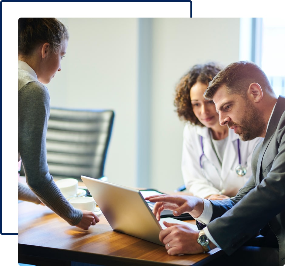 A doctor having a discussion with a man in a suit as they look at a laptop and a woman serves them coffee.