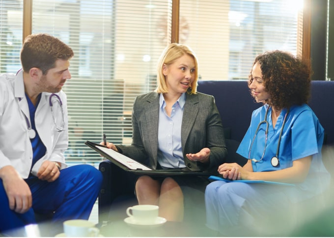 A male and female doctor sitting and having a discussion with a blond woman in a business suit.