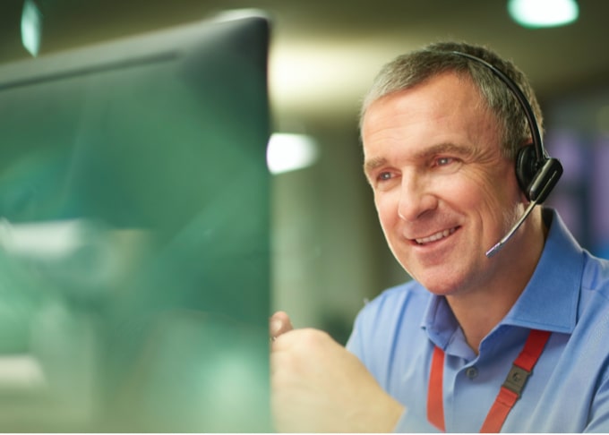 A smiling man working on a computer with headphones on.